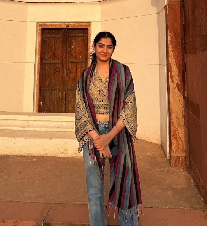 Portrait of Sayantani Mukherjee standing in front of a wooden door in warm evening light